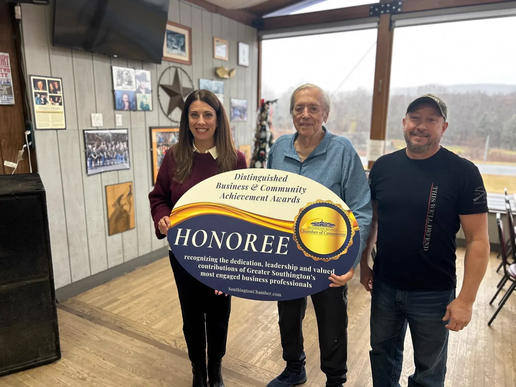 Graham Nicholson at Cadillac Ranch holding the Southington Regional Chamber of Commerce Distinguished Business and Community Achievement Awards honoree sign, flanked by two people.