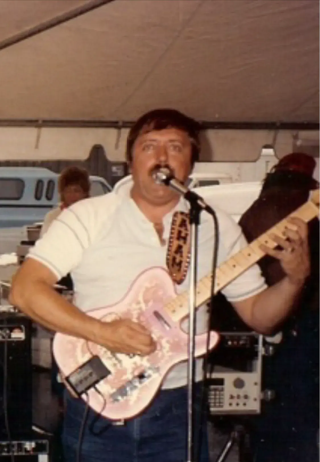 Graham Nicholson singing at a tent gig with his pink paisley Telecaster on a tooled leather strap stamped with his name.