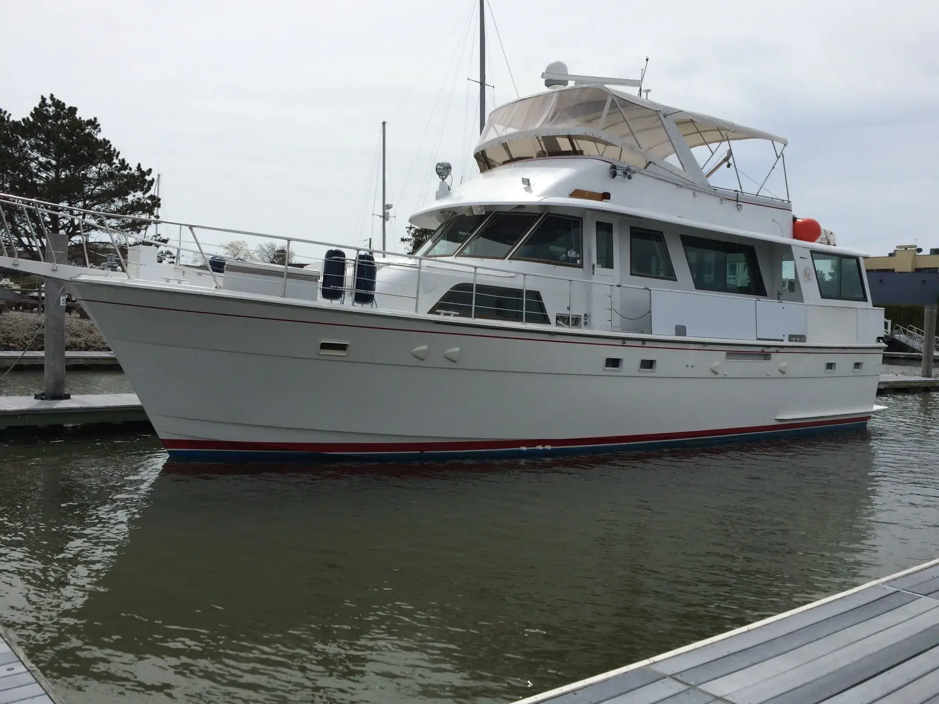 The charter motor yacht alongside a floating dock: white hull with a red boot stripe, flybridge under a cream bimini.