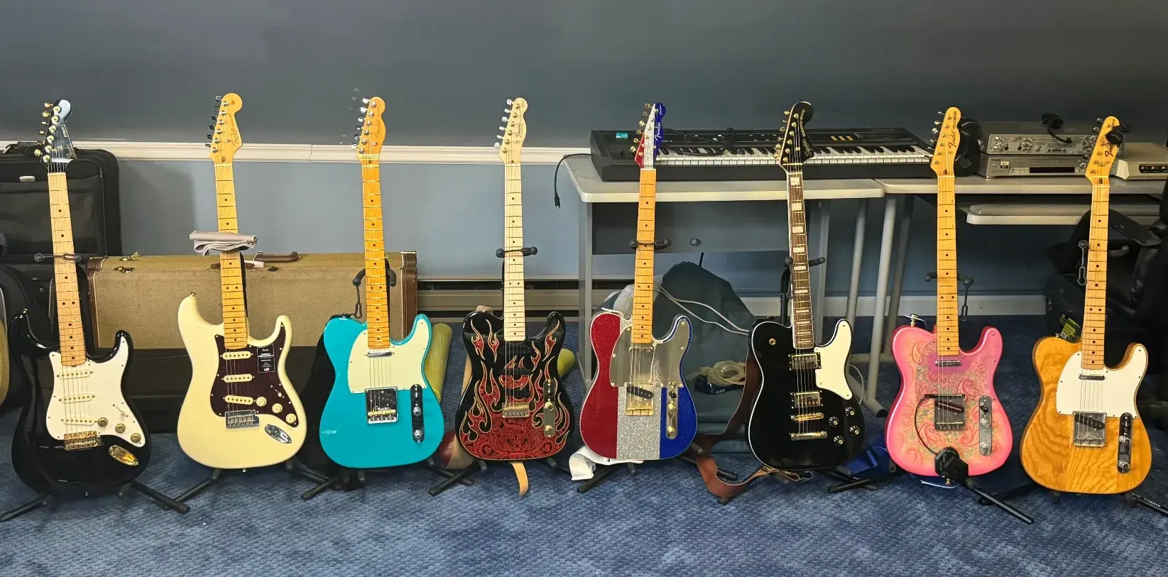 A long line of Graham Nicholson's guitars stood against a wall outdoors — Telecasters, Stratocasters and paisley-finish guitars among them.