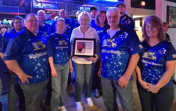 A group in blue Wishes on Wheels shirts at the Cadillac Ranch bar, one of them holding a framed appreciation award.