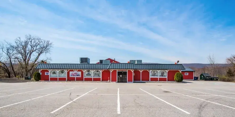 The long red exterior of the Cadillac Ranch Restaurant in Southington by day, with its parking lot in front.