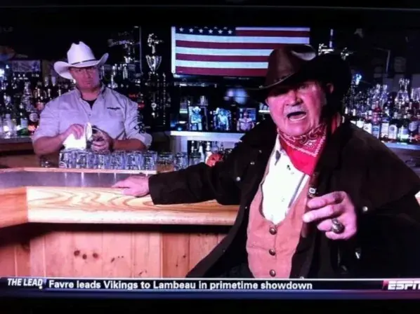 Two men in cowboy hats at the Cadillac Ranch bar, a television showing a football game behind them.