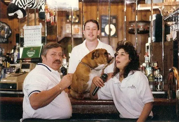 Three people behind the Cadillac Ranch bar, one of them holding a bulldog.
