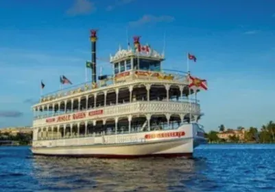 A large multi-deck riverboat tour vessel flying flags, underway on open water.