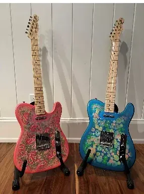 Two paisley-finish Fender Telecasters standing side by side, one pink, one blue.