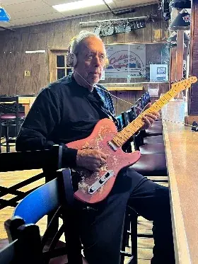 Graham Nicholson seated at the Cadillac Ranch, playing his pink paisley Telecaster.